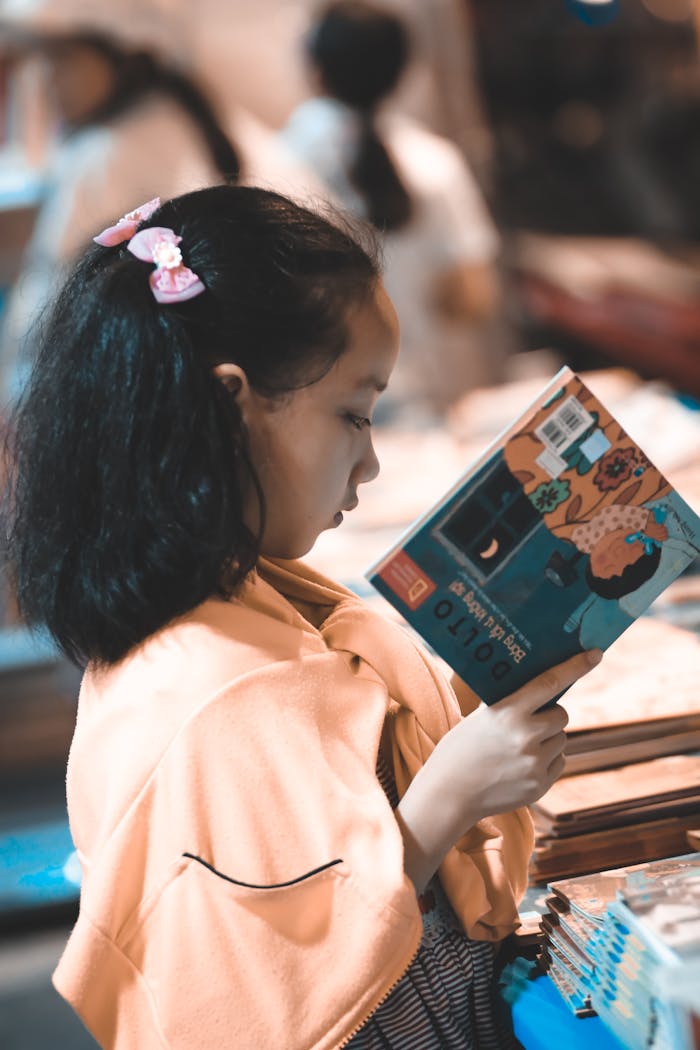 Focused young girl reading a colorful book indoors, perfect for educational themes.